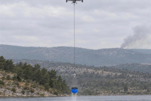 Firefighting bucket under a heavy firefighting drone scooping from a mountain lake