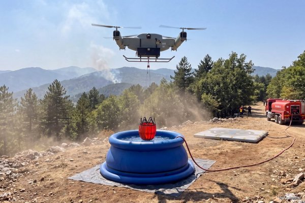 Firefighting drone dipping its bucket into the reservoir beside a forest track